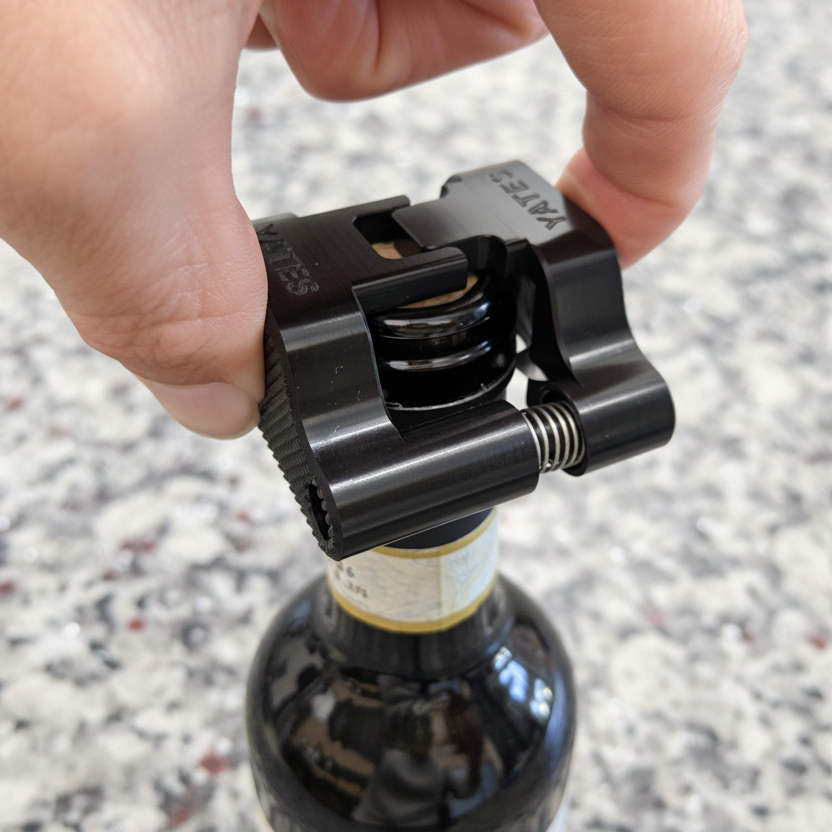 A close up photo of a hand holding the Yates foil cutter using just two fingers, and using the foil cutter to cut the foil on the top of the wine bottle.